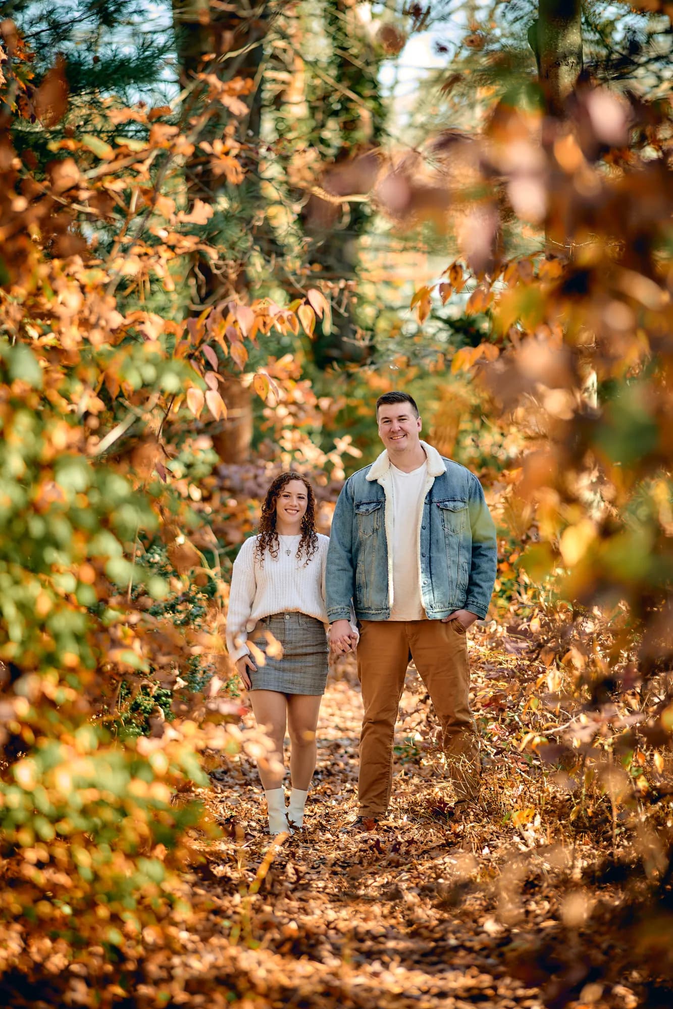 Couple walking a leaf-covered trail framed by glowing autumn foliage