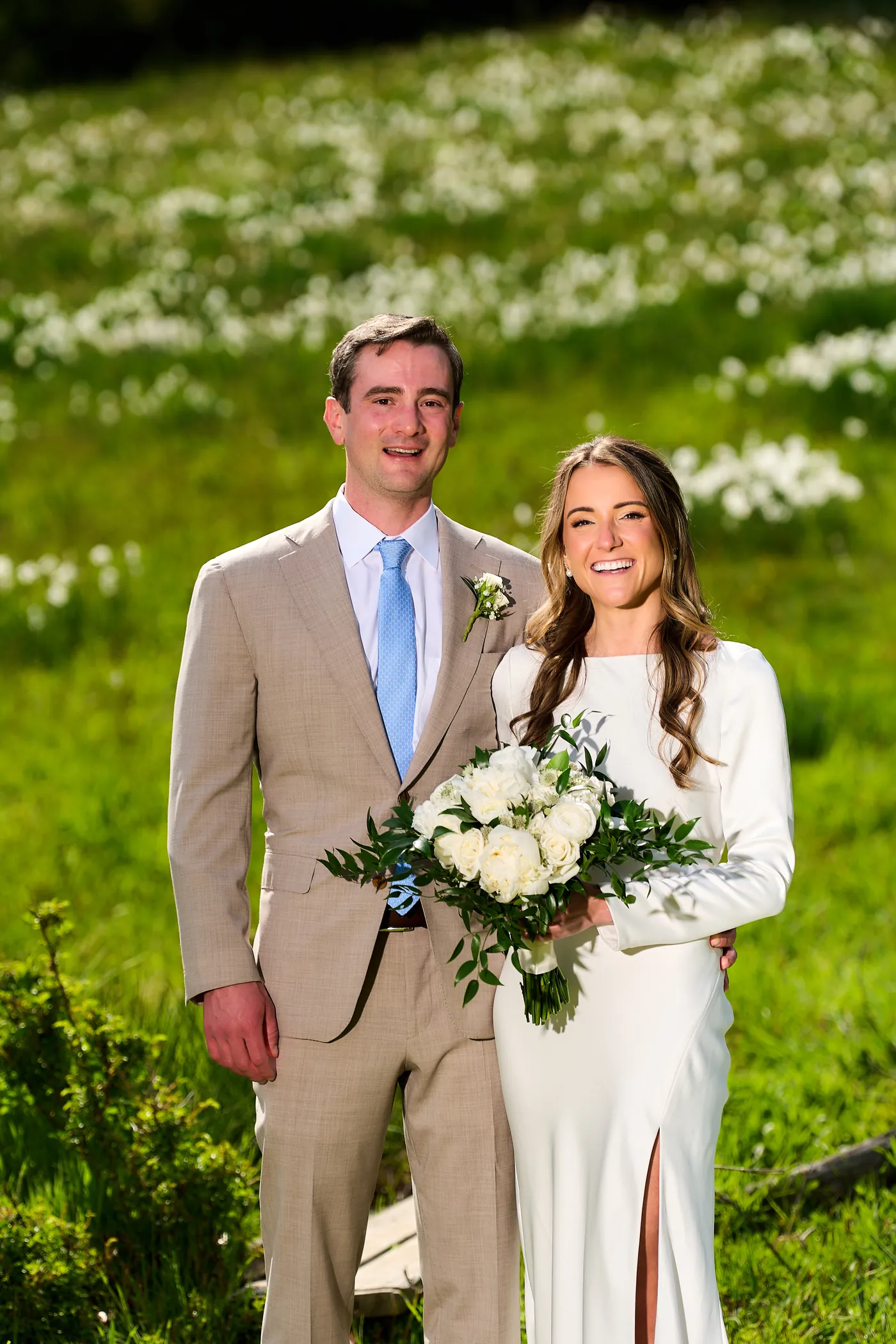 Engaged couple in a grassy meadow with soft greenery behind them