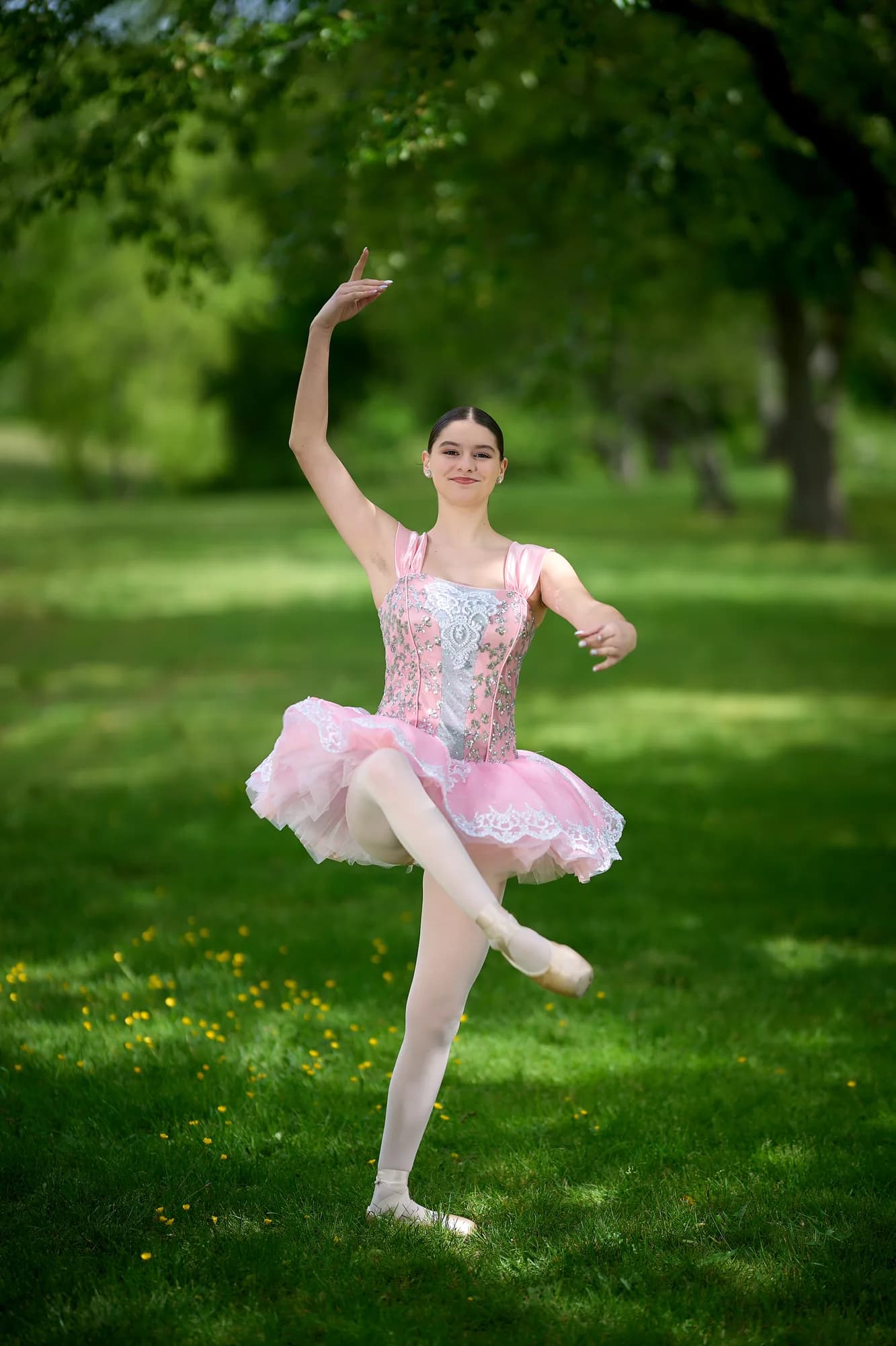 Young ballerina in a pink tutu posing on point in a sunlit park
