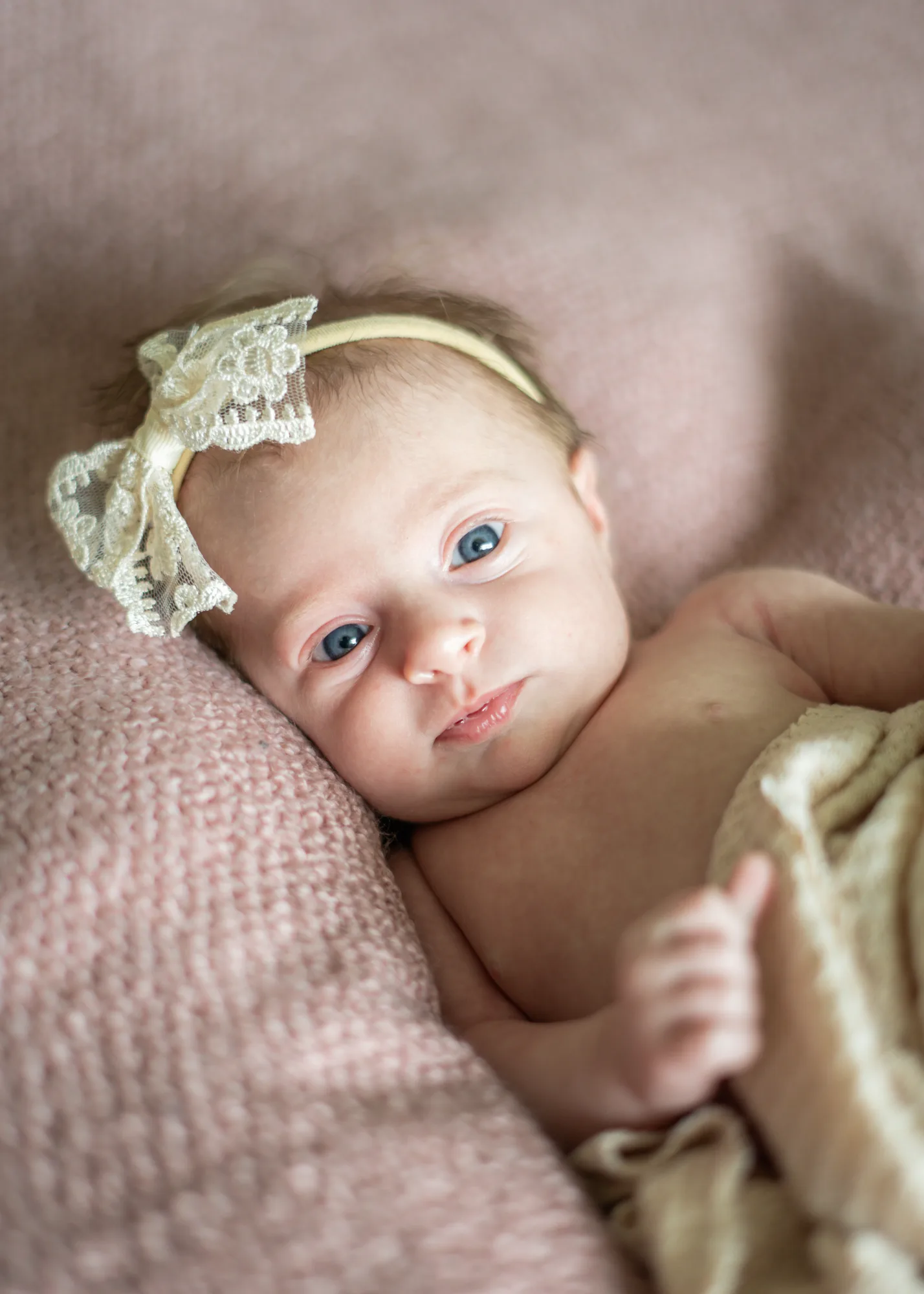 Newborn baby girl with a lace bow resting on a soft pink blanket