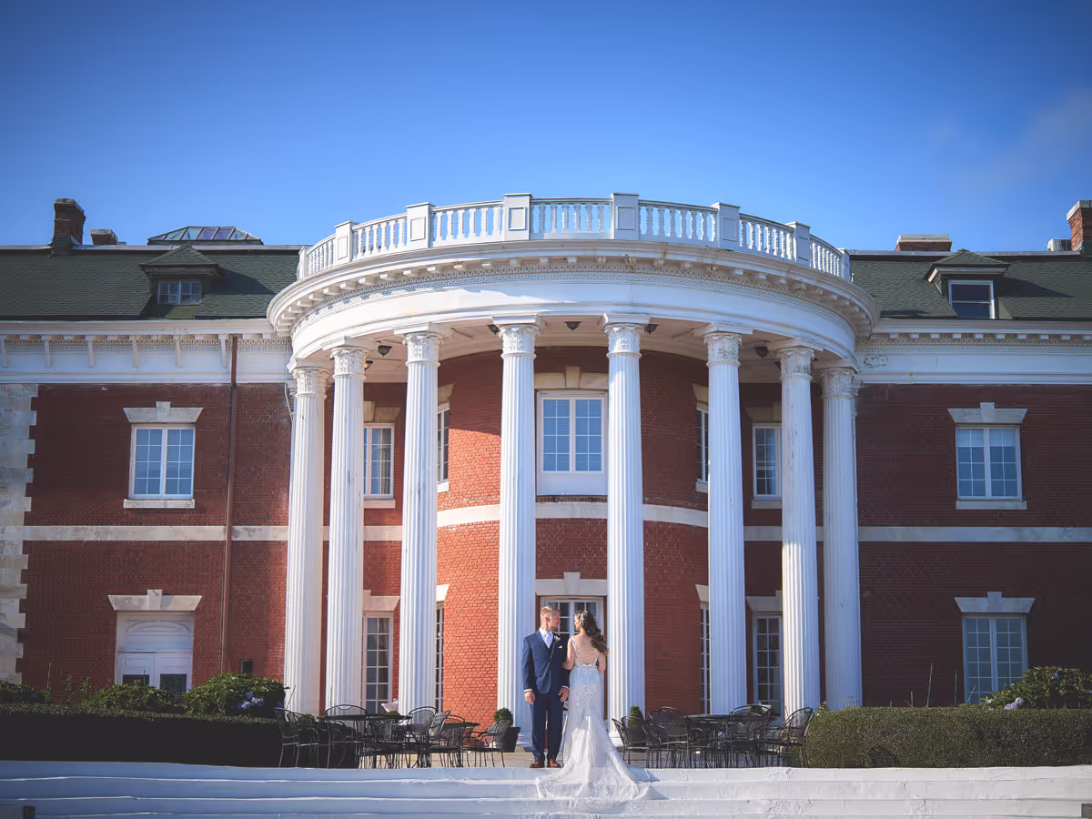 Spring blossoms against autumn vines, Couple framed by the columned facade of a grand Long Island mansion venue