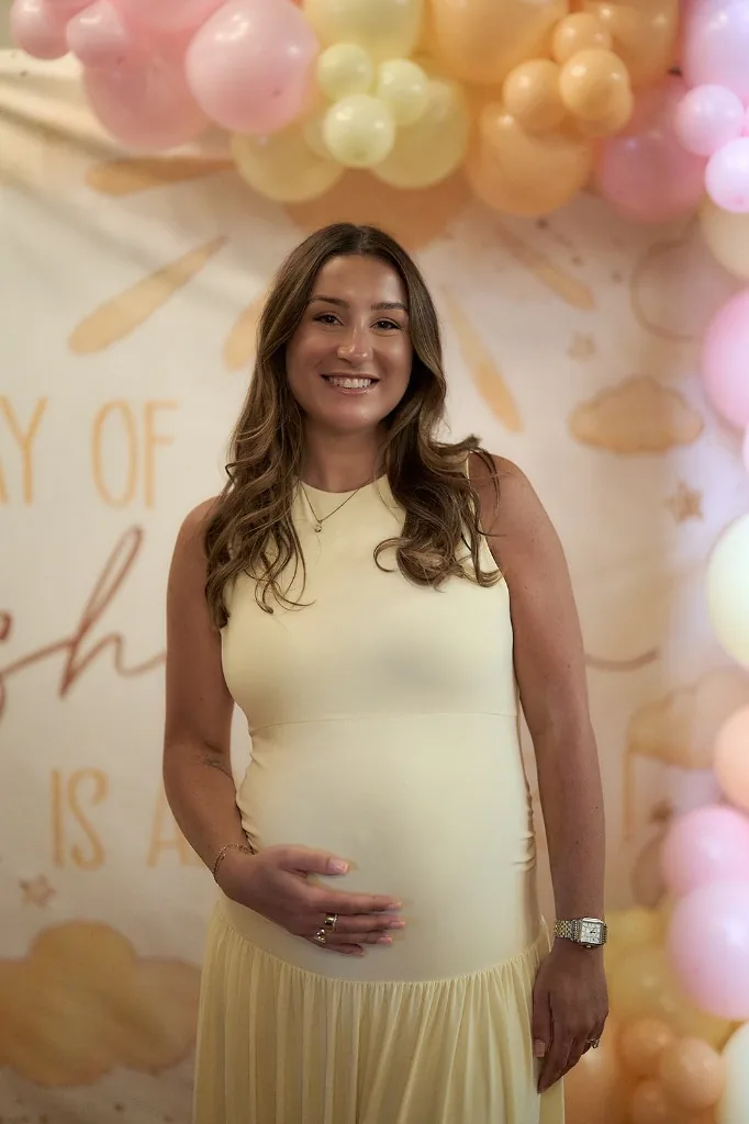 Expecting mother in a soft yellow dress beside a pastel balloon arch