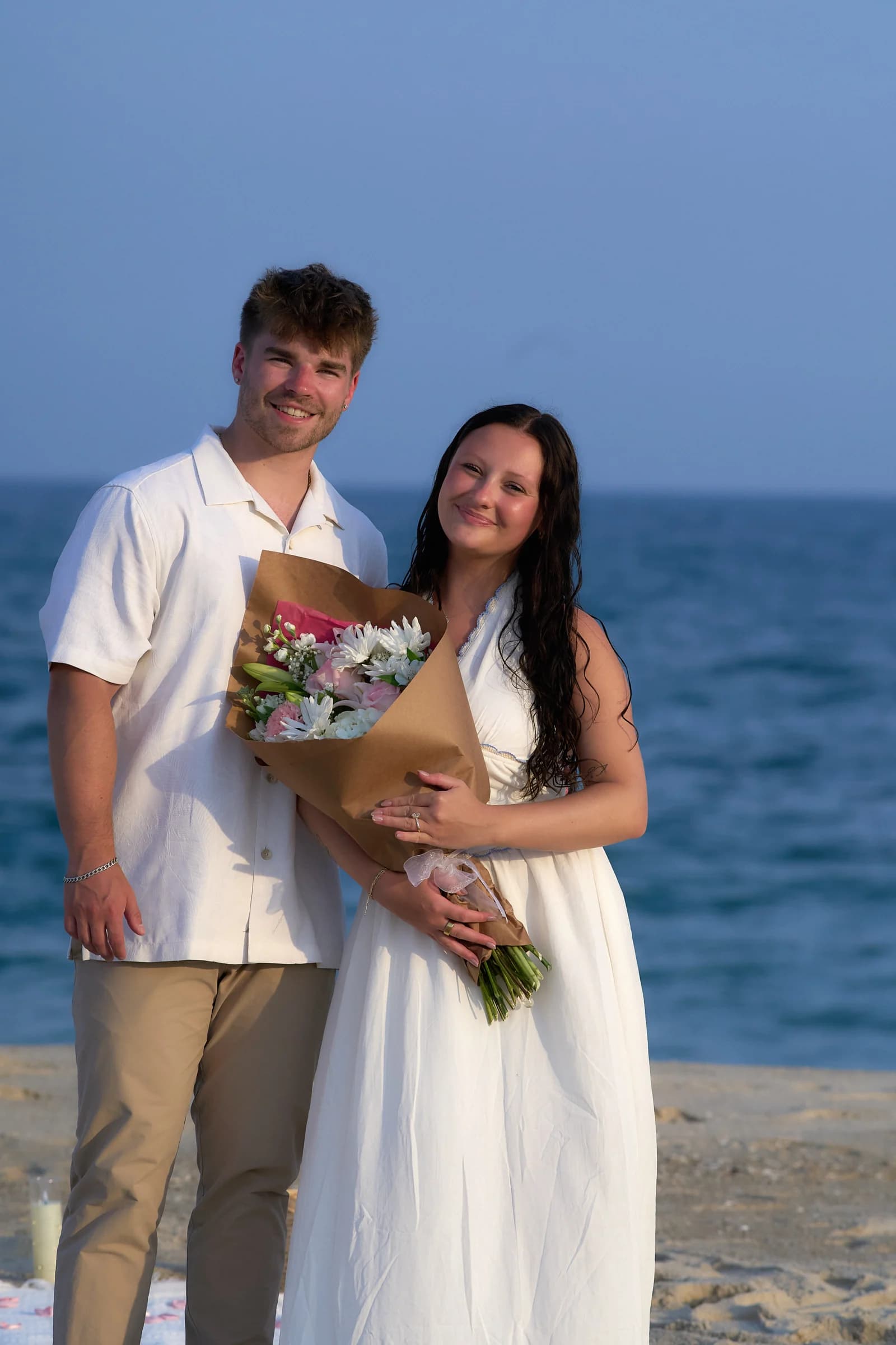 Athena and Tristan on the beach with her bouquet after the proposal