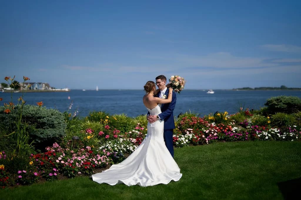 Cinematic film beside a vertical phone clip, Full length portrait of the bride and groom on the garden patio with the bay behind them at the Riviera