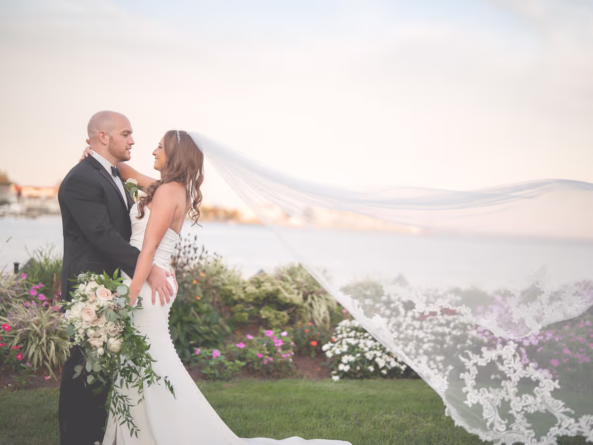 Bride and groom at golden hour by the water, the bride's veil catching the wind at a Long Island wedding