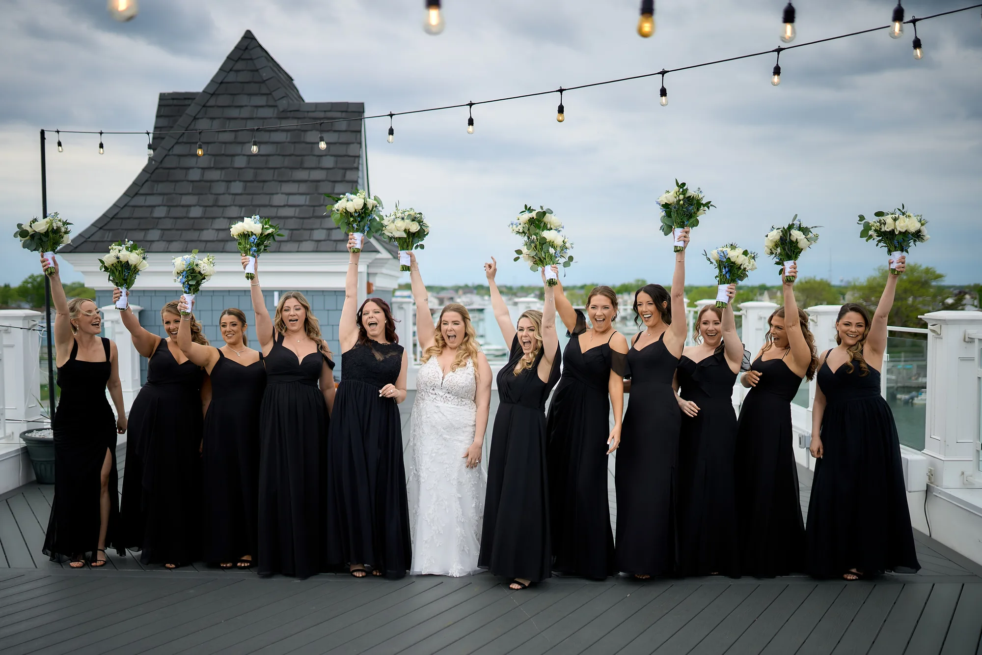 A fine art album open on a table, Bride and her bridesmaids in black gowns cheering with bouquets on a rooftop terrace