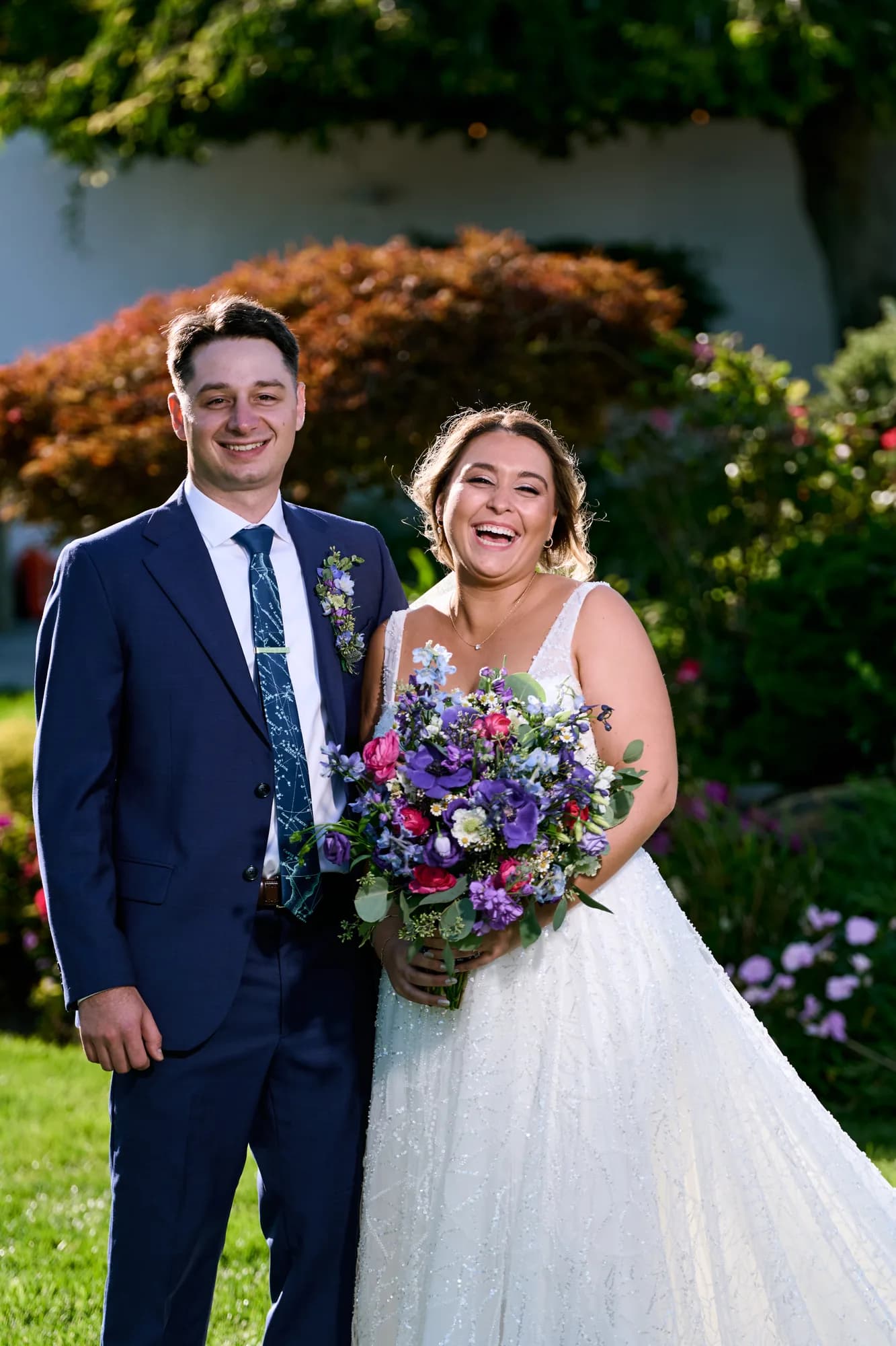 Grand staircase against park grounds, Bride laughing beside her groom while holding a colorful wildflower bouquet