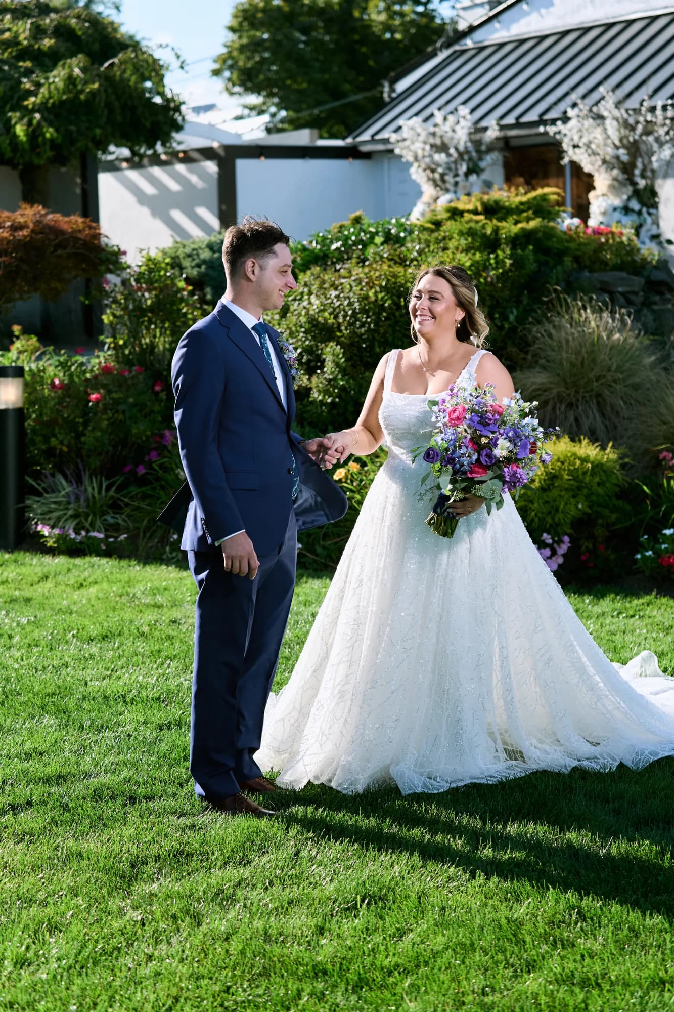 Beach sunset against a garden path, Bride and groom walking hand in hand across a green venue lawn