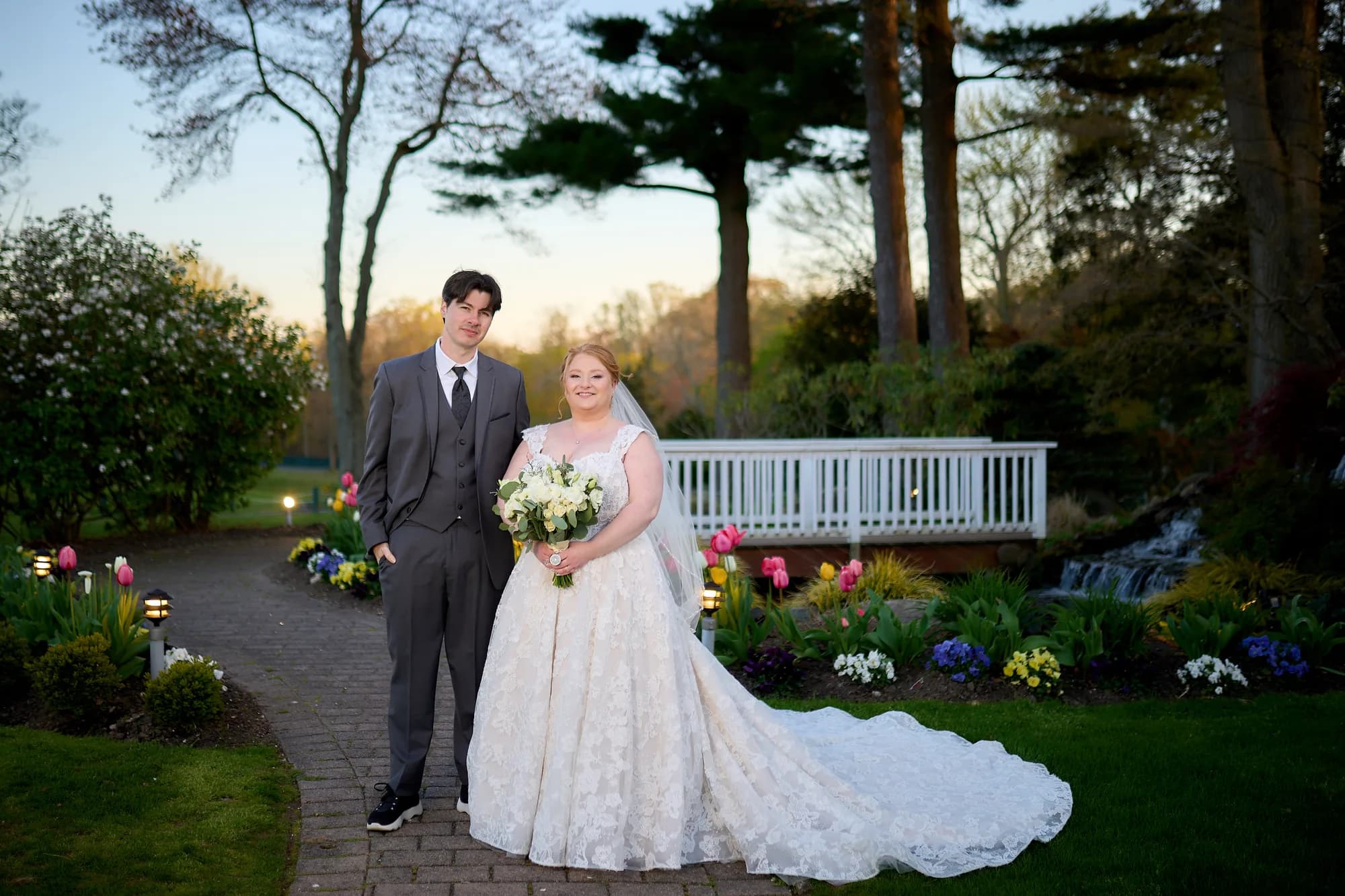 Croteaux Vineyards, Southold, Bride with a long gown train and her groom on a garden path at sunset