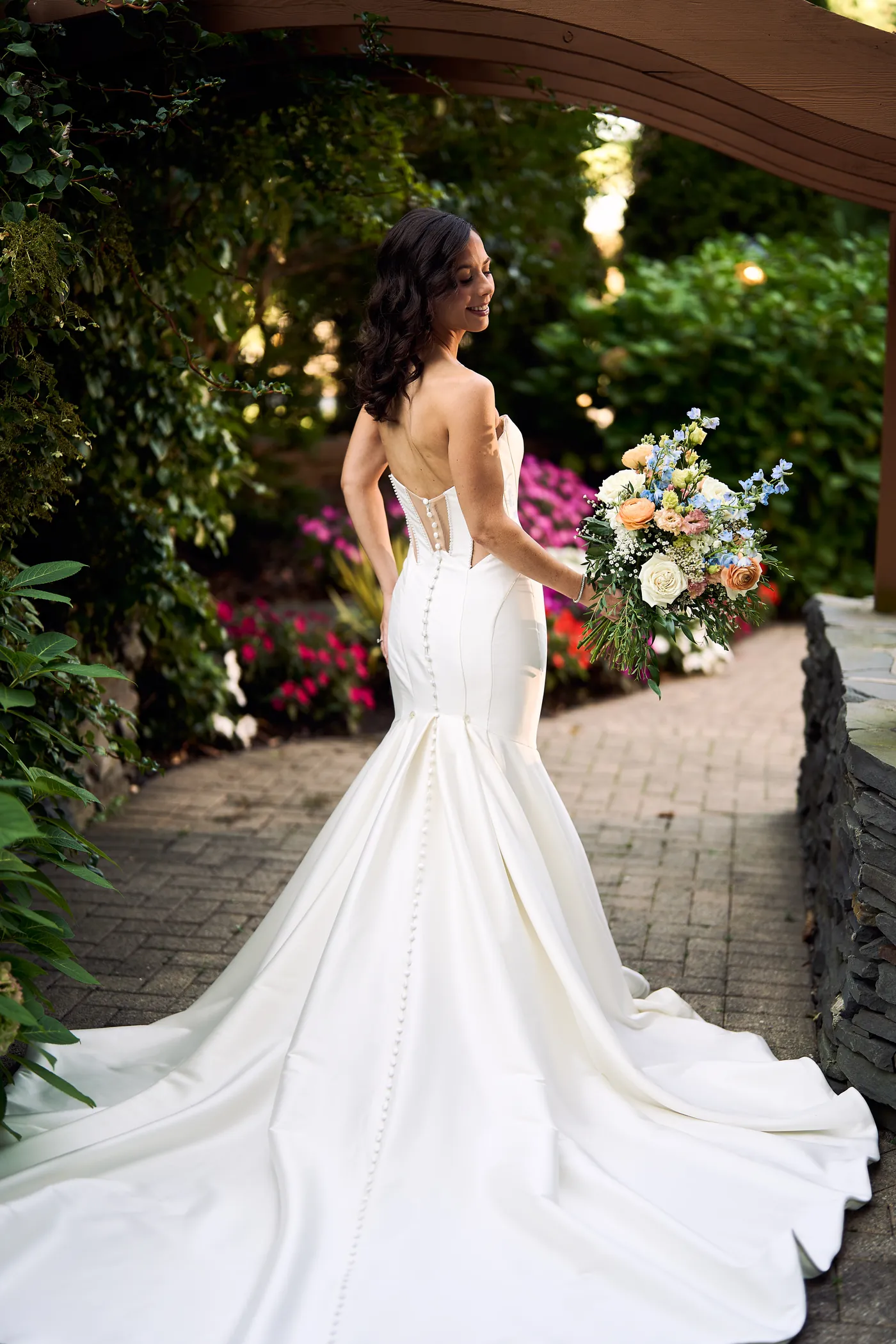 Chandelier light against open air ceremony, Back of a fitted wedding gown with a long train in a manicured garden