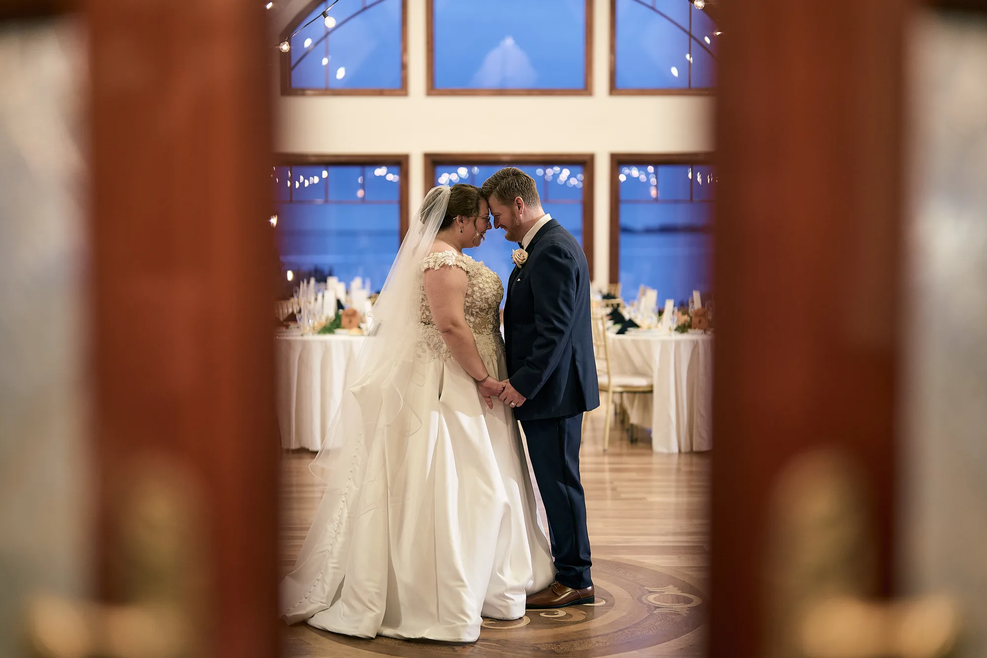 Estate facade against a grand ballroom, Bride and groom framed in an open doorway of a waterfront reception room