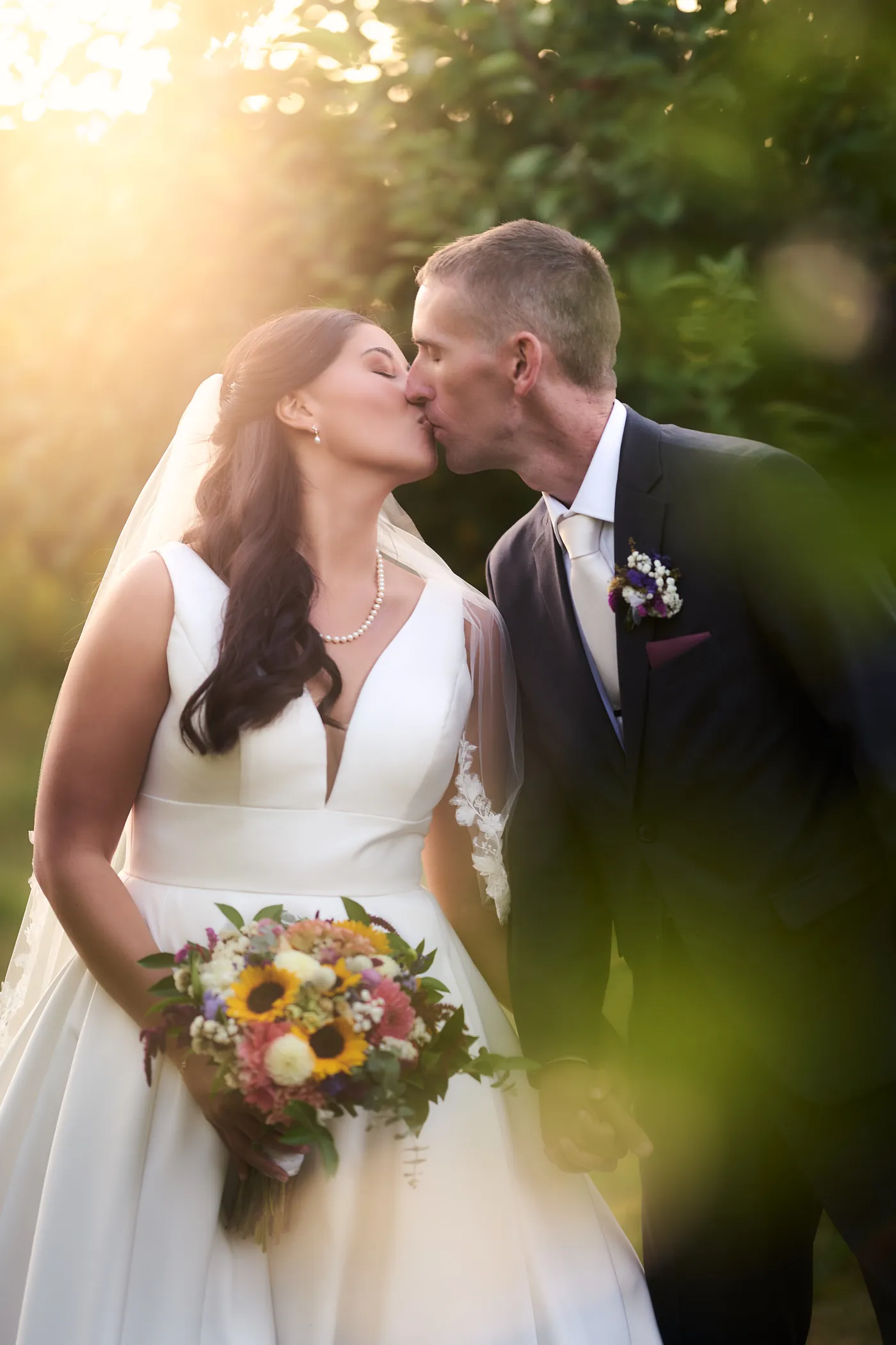 Vineyard rows against a bayfront terrace, Bride and groom kiss in warm backlit sunset glow