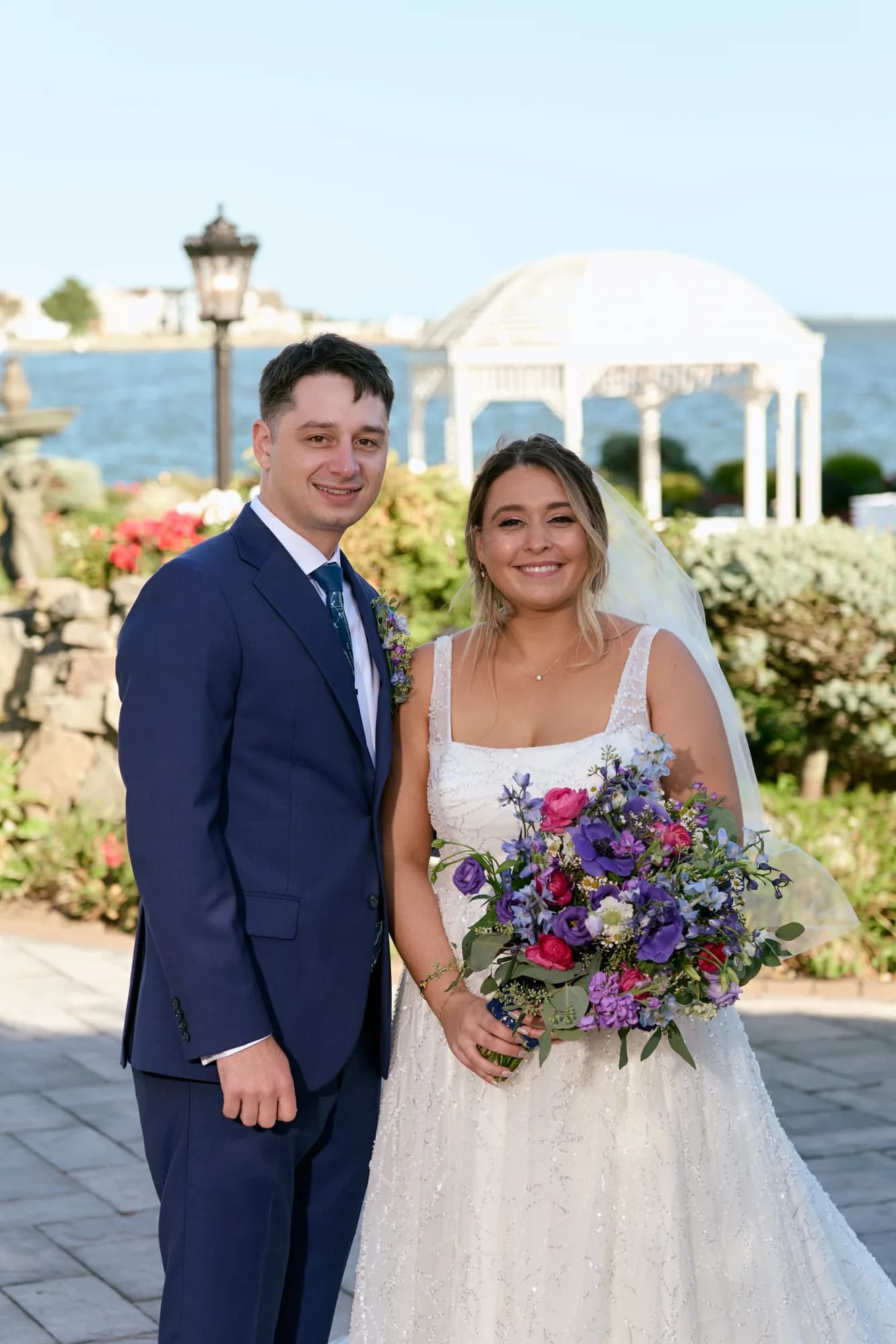 Bride and groom beside a white gazebo with the bay behind them